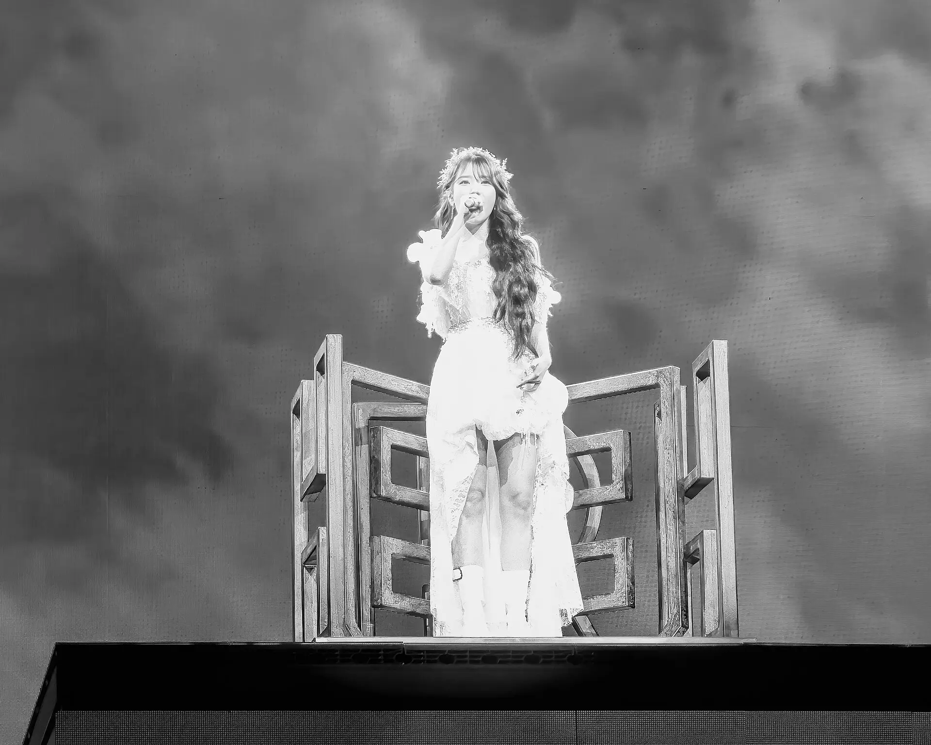 IU singing on a tall stage set during her HEREH world tour, in black and white