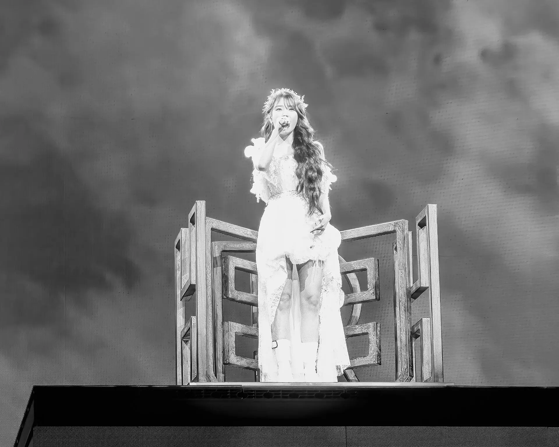IU singing on a tall stage set during her HEREH world tour, in black and white