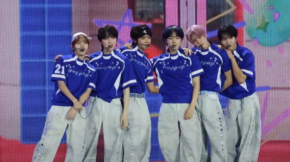 NCT WISH members in matching blue and white outfits posing on a music show stage