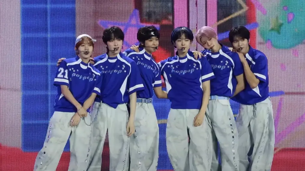 NCT WISH members in matching blue and white outfits posing on a music show stage