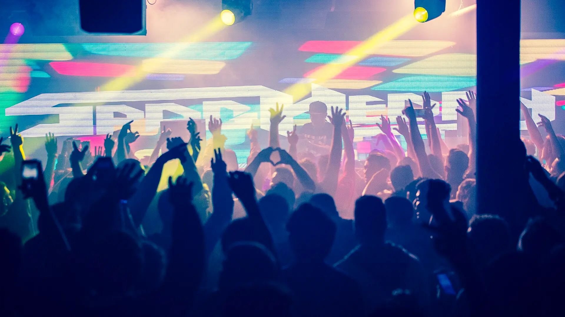 A concert crowd in silhouette with hands raised under stage lights