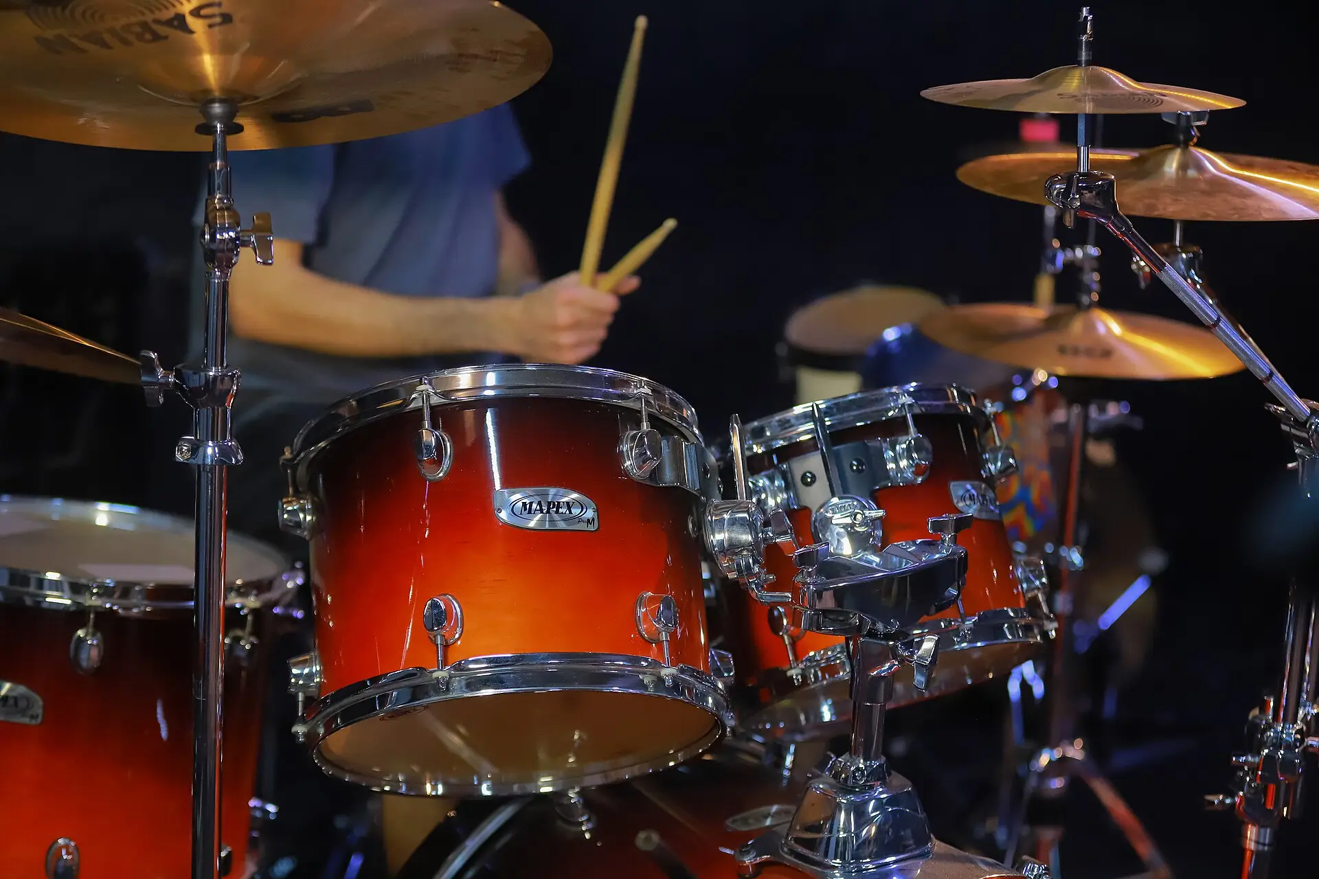 Close-up of a red drum kit and cymbals being played on a dark stage